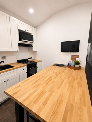 Una cocina moderna con armarios blancos, encimera de madera, estufa y televisor de pantalla plana montado en la pared.