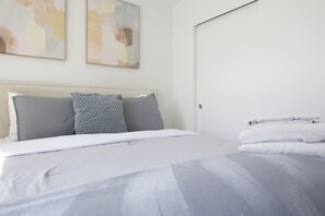 A neatly made bed with a white comforter and pillows, a folded white towel on the side, and abstract art on the wall. - Ballard Bright Modern Townhome w/ Rooftop Deck (Seattle)