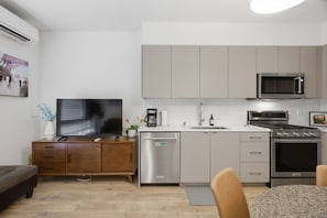 Ett modernt kök med diskmaskin, mikrovågsugn, spis och en matplats med bord och stolar.