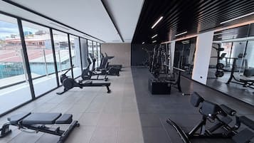 Une salle de sport moderne équipée de machines de cardio, d’appareils de musculation et de grandes fenêtres offrant une vue sur la ville.