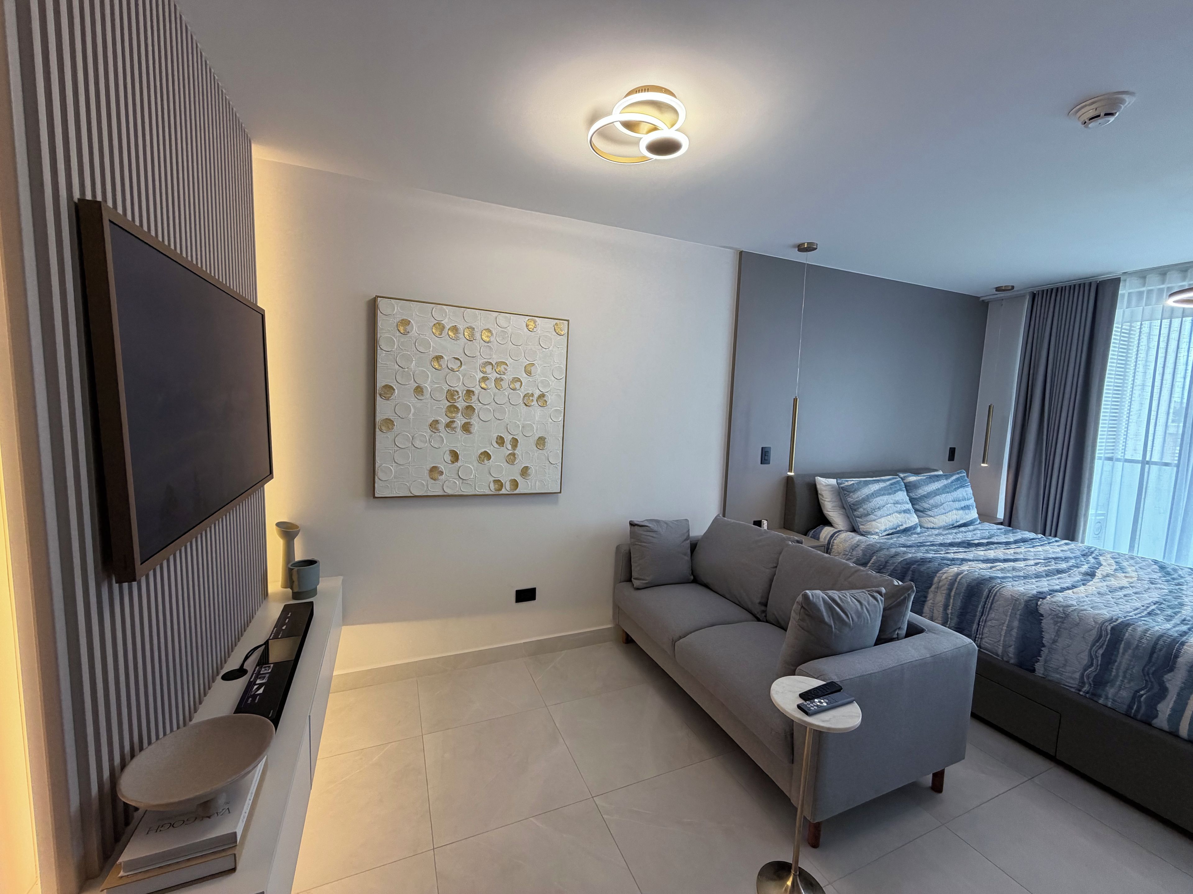 Une chambre moderne dotée d’un téléviseur à écran plat, d’un canapé, d’un lit avec une literie à motifs et d’un élément décoratif mural.