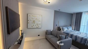 Une chambre moderne dotée d’un téléviseur à écran plat, d’un canapé, d’un lit avec une literie à motifs et d’un élément décoratif mural.