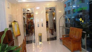 Un vestíbul d'hotel amb una recepció, una banca de fusta i un ascensor de vidre.