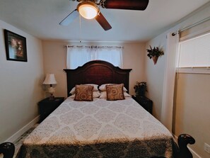 A bedroom with a bed, a nightstand, a lamp, a ceiling fan, a window with blinds, and a wall-mounted plant. - Bonita Home- Charming 3-bedroom house with AC in scenic Twin Falls (Twin Falls)