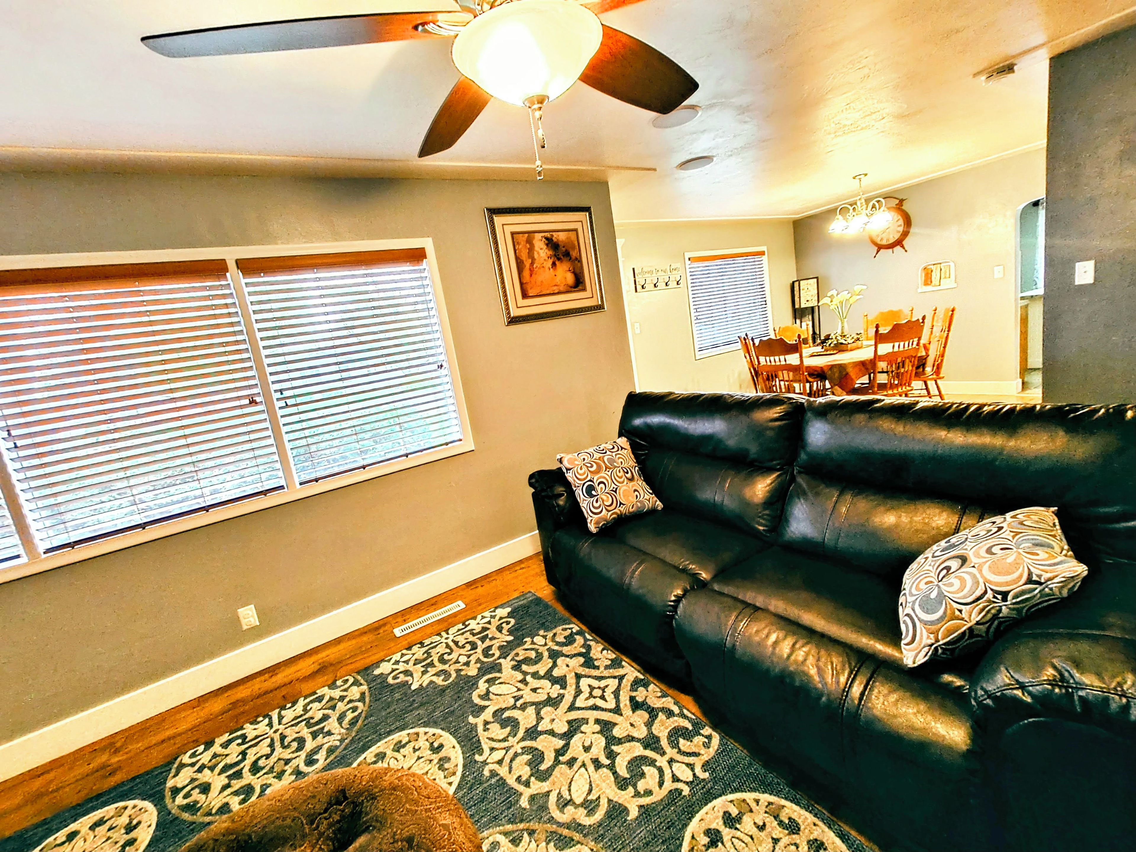A living room with a black leather sofa, patterned rug, and a ceiling fan.