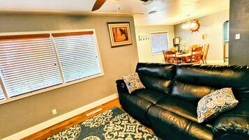 A living room with a black leather sofa, patterned rug, and a ceiling fan.