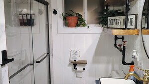 Een badkamer met een douchecabine van glas, een toilet, een wastafel met spiegel en een plank met een potplant.