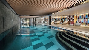 Una piscina interior moderna con suelo a cuadros, zonas de descanso con tumbonas y techo de madera.