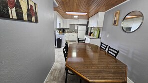 A dining area with a wooden table and chairs, a kitchen in the background, and a skylight above. - Comfy 3BD Dog Friendly home! (Colorado Springs)