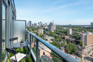 Ein Balkon mit Tisch und Stühlen mit Blick auf eine Stadtlandschaft mit Gebäuden und Grünflächen.