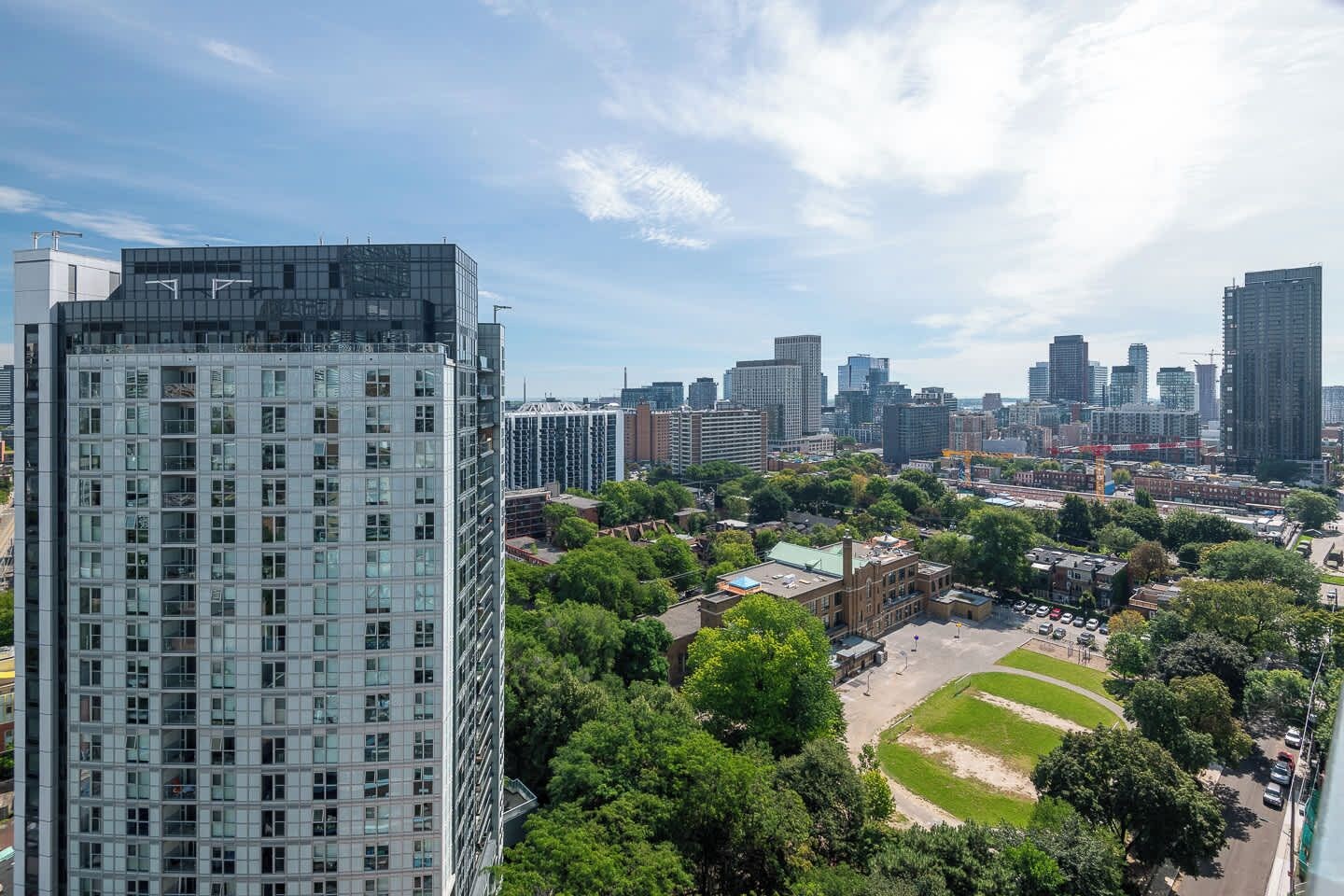A high-rise building with a grid of windows, surrounded by a park area with trees and a small building.