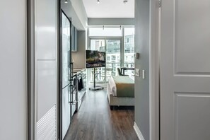Een moderne hotelkamer met een groot bed, een balkon met uitzicht op de stad, een kitchenette en een televisie.
