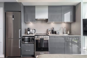 Een moderne keuken met roestvrijstalen apparatuur, grijze kastjes en een betegelde achterwand.