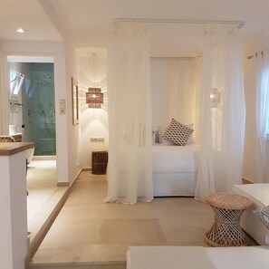 A modern bedroom with a bed, a bedside table, a woven stool, and a shower area. - Kavos Boutique Hotel Naxos (Naxos)