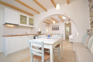 A kitchen with white cabinets, a dining table, and a stone wall. - Kavos Boutique Hotel Naxos (Naxos)