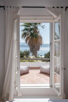 Una habitación con un ventanal grande, cortinas blancas y vistas a una palmera y al mar.