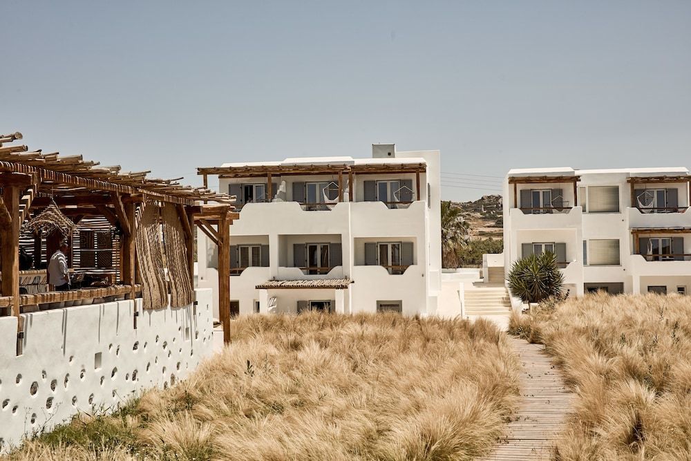 A coastal building with multiple balconies, a wooden pergola, and a pathway leading to the entrance.