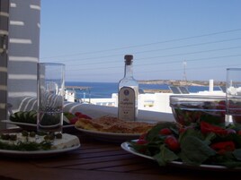 Una mesa con platos de comida, una botella y vasos, con vista al mar.