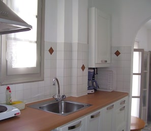 Una cocina con un lavamanos de acero inoxidable, armarios blancos y una ventana sobre el lavamanos.