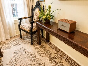 A room with a floral-patterned chair, a wooden side table with a vintage radio, and a patterned carpet.