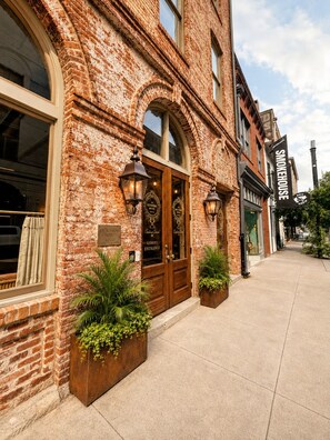 A brick building with a wooden entrance door, two potted plants, and a sign for 'The Redstone Hotel'.