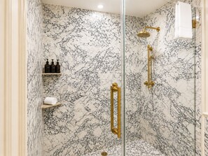 A bathroom with a marble wall, a glass shower enclosure, and a gold showerhead.
