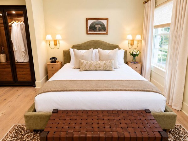 Une chambre d’hôtel avec un grand lit, deux tables de chevet avec des lampes, une armoire et une fenêtre avec des rideaux.