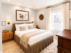 A bedroom with a large bed, bedside tables, a nightstand, a lamp, a framed picture on the wall, a window with curtains, and a wooden dresser. - Ethan's Room at Keystone Hotel - 207 (Savannah)