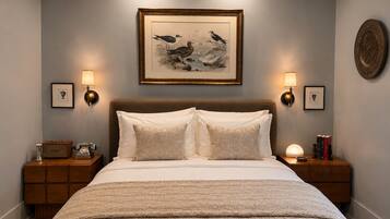 Quarto com uma cama grande, duas mesas de cabeceira, uma obra de arte emoldurada sobre a cama e arandelas de parede.