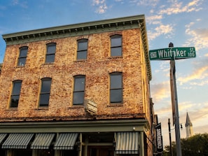 A brick building with a green awning and a street sign for Whitaker St. 100. - Ethan's Room at Keystone Hotel - 207 (Savannah)