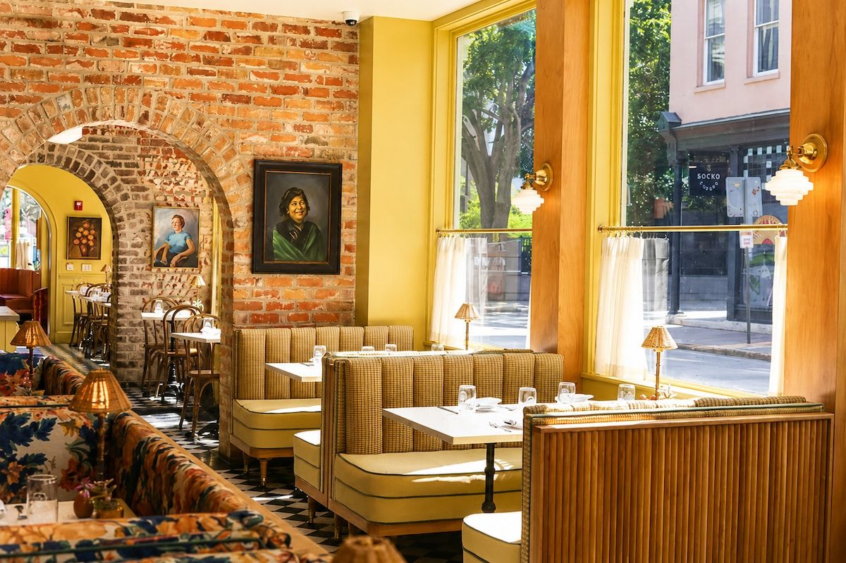 Um restaurante com paredes de tijolo, detalhes em amarelo e um espaço de estar acolhedor com mesas e cadeiras.