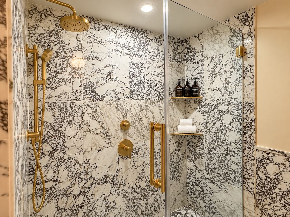 A bathroom with a glass-enclosed shower, marble walls, and a shelf with toiletries.