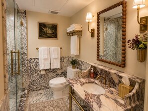 A bathroom with a marble sink, a toilet, and a glass-enclosed shower. There are towels and a framed picture on the wall. - Ethan's Room at Keystone Hotel - 207 (Savannah)