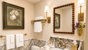 Ein Badezimmer mit Marmorwaschtisch, goldenen Armaturen, einer Toilette und einem gerahmten Blumenbild an der Wand.