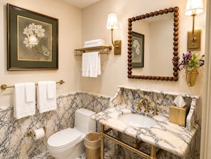 A bathroom with a marble sink, gold fixtures, a toilet, and a framed floral artwork on the wall. - Uncle Jack's Room at Keystone - 204 (Savannah)