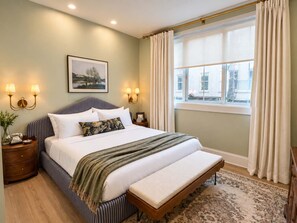 A hotel room with a large bed, bedside lamps, a window with curtains, and a framed picture on the wall.