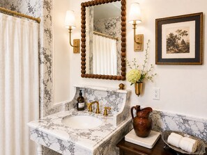 A bathroom with a marble sink, a mirror with wall sconces, a framed picture, and a vase with flowers. - Aunt Rachel's Room at Keystone - 203 (Savannah)