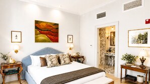 Um quarto com cama, mesas de cabeceira, um banco e obras de arte nas paredes.