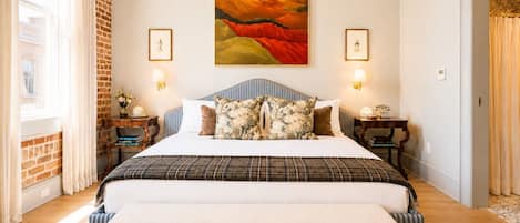 A spacious bedroom with a large bed, a brick wall, and a painting above the bed.