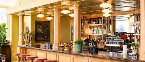 A bar area with stools, a counter, and a variety of bottles and glasses.