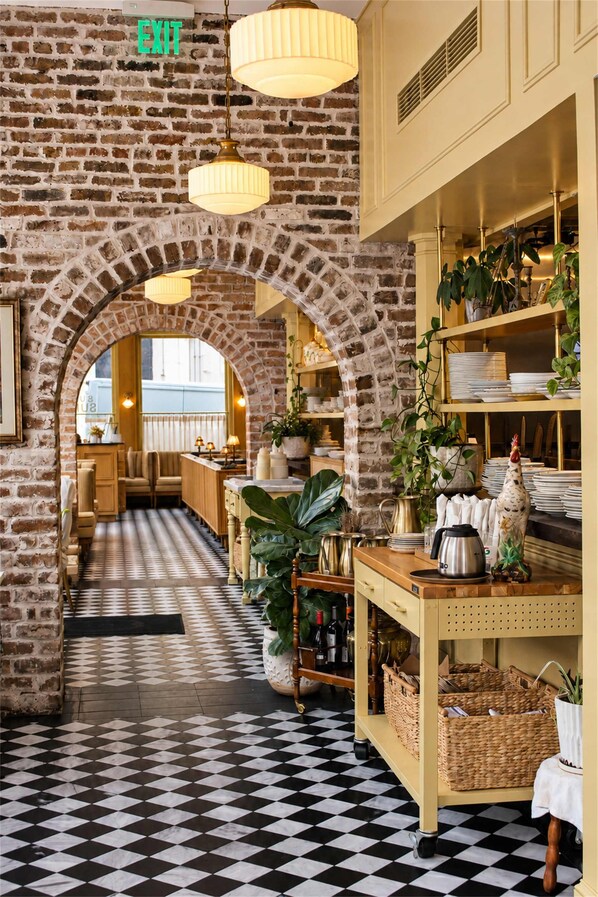 A restaurant interior with brick walls, a checkered floor, and a central archway leading to the dining area.