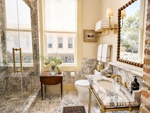 A bathroom with a marble sink, a glass shower enclosure, and a view of the outside. - Neiman's Room at Keystone Hotel - 202 (Savannah)