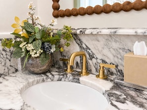 A bathroom sink with a marble countertop, a gold faucet, and a vase of flowers. - Grandma's Room at Keystone | Downtown Savannah (Savannah)