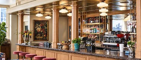 A bar area with a marble countertop, multiple stools, a variety of bottles, and a coffee machine.