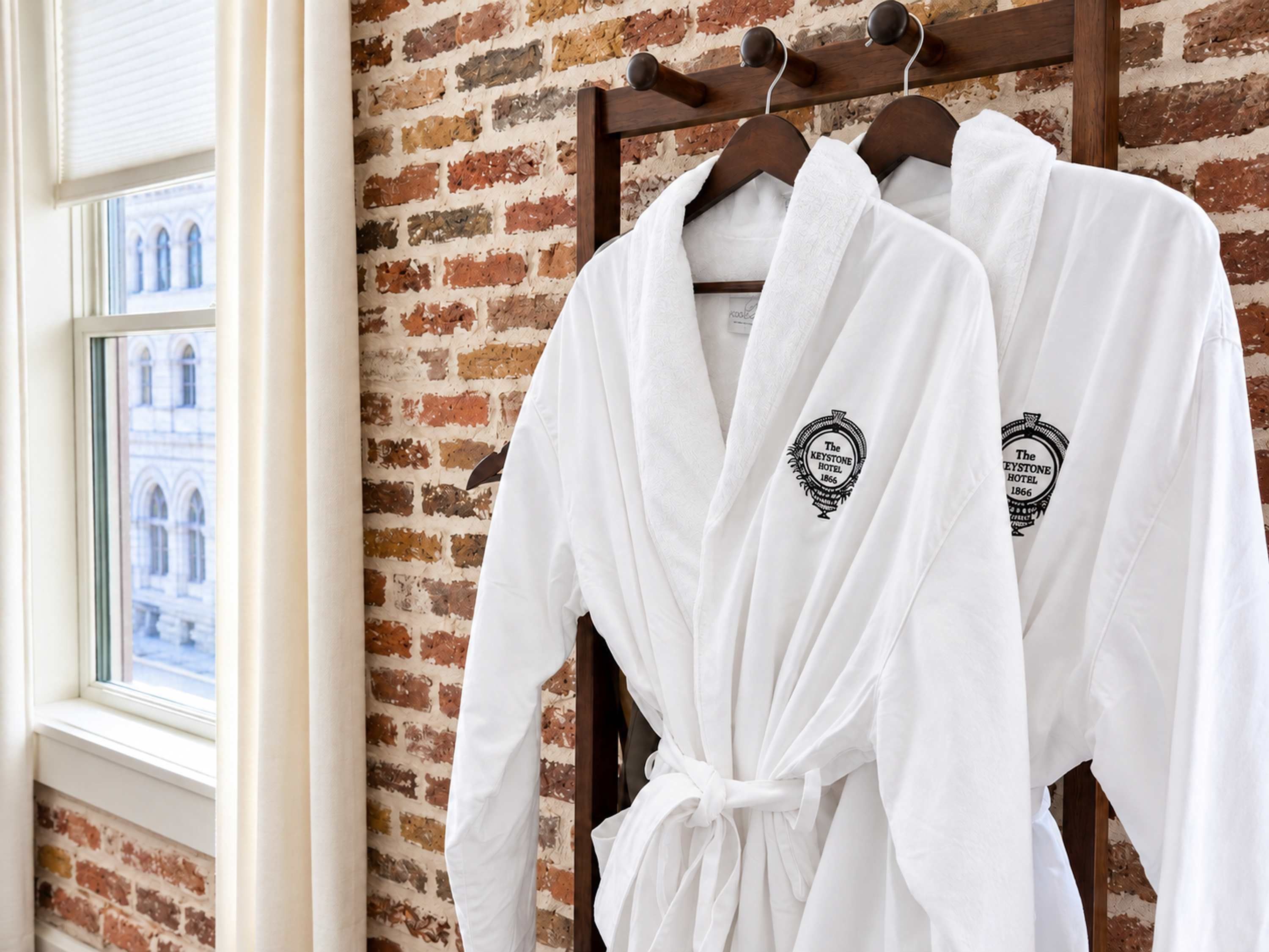 Two white robes hanging on a wooden rack against a brick wall.