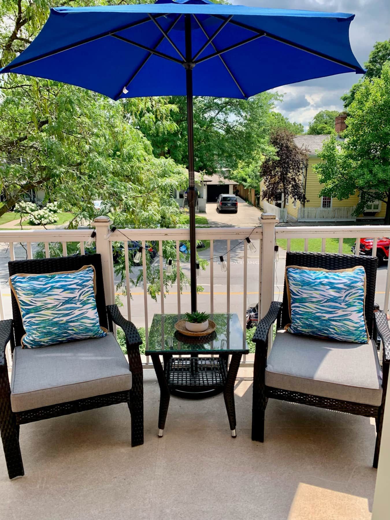 A balcony with two chairs, a small table, and a blue umbrella.