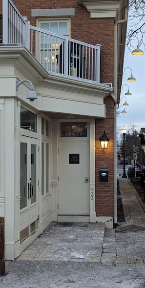 A building with a white facade, a balcony with railings, a door labeled 'SUITES KING,' and a brick wall. - The Diana Suite - Elegant and Serene (Niagara-on-the-Lake)