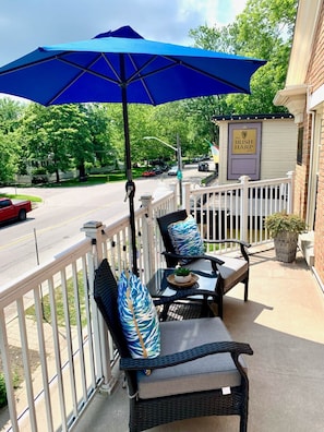 A covered outdoor seating area with two wicker chairs and a blue umbrella, a small sign for 'The Irish Harp Pub', and a street view in the background. - The Diana Suite - Elegant and Serene (Niagara-on-the-Lake)