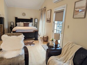 A bedroom with a bed, a bedside table with a lamp, a chair, and a window with curtains. - The Lilibet Suite - Regal and Royal (Niagara-on-the-Lake)