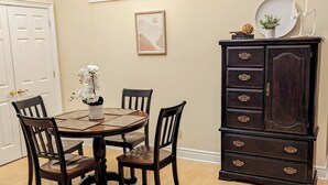 Un coin repas avec une table ronde, quatre chaises, un buffet en bois foncé doté de tiroirs, un tableau encadré accroché au mur et une fenêtre au-dessus de la table.